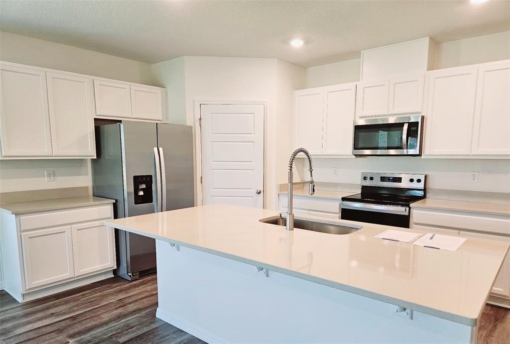 A modern kitchen features white cabinets, stainless steel appliances, and a large central island — 1237 LIMBALI STREET, MOUNT DORA, FL