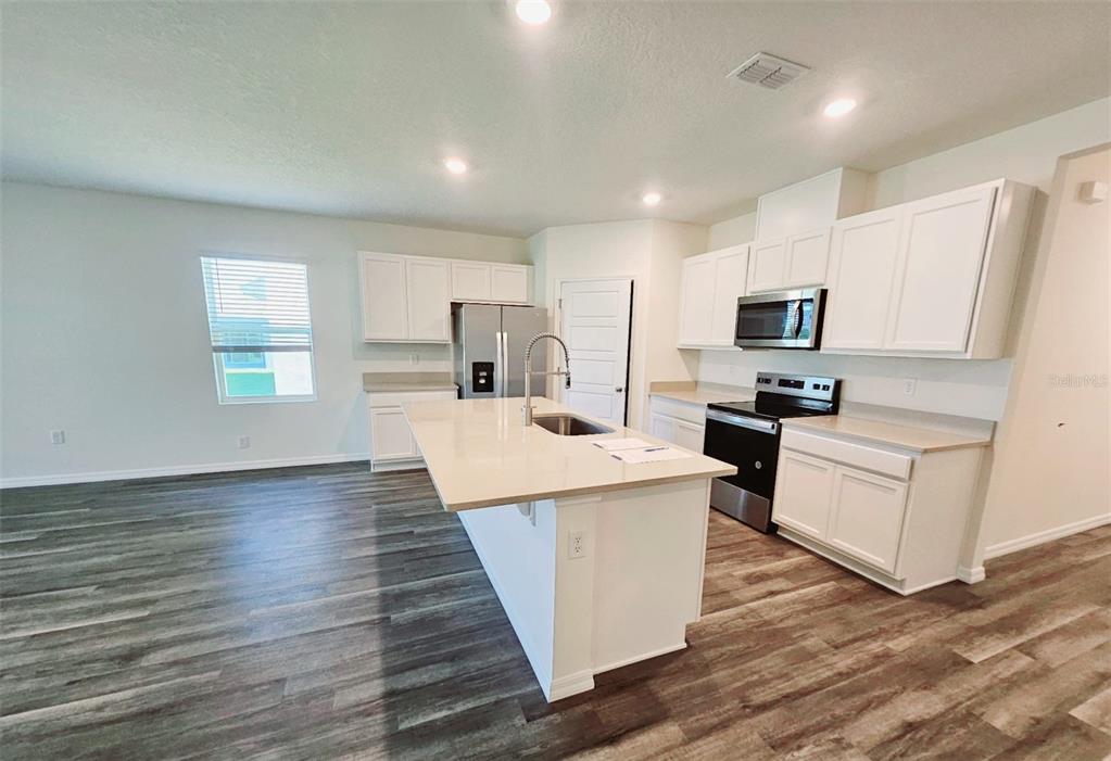A modern kitchen features white cabinets, quartz countertops, a center island, and wood-look flooring — 1237 LIMBALI STREET, MOUNT DORA, FL