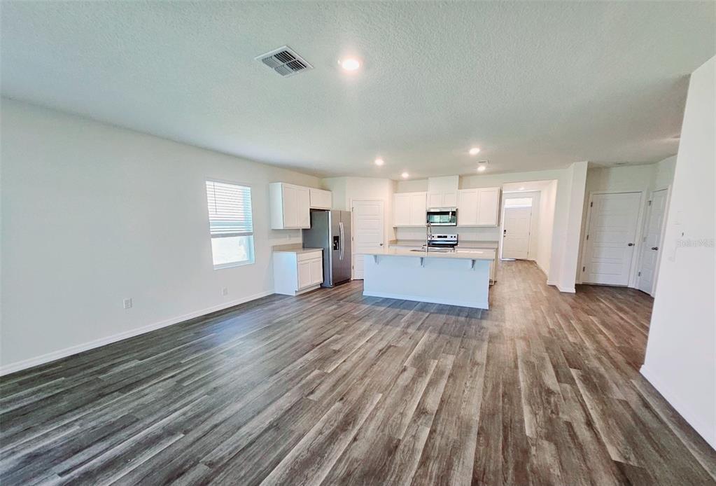 An open-concept kitchen and living area with white cabinetry, a central island, and wood-look flooring — 1237 LIMBALI STREET, MOUNT DORA, FL