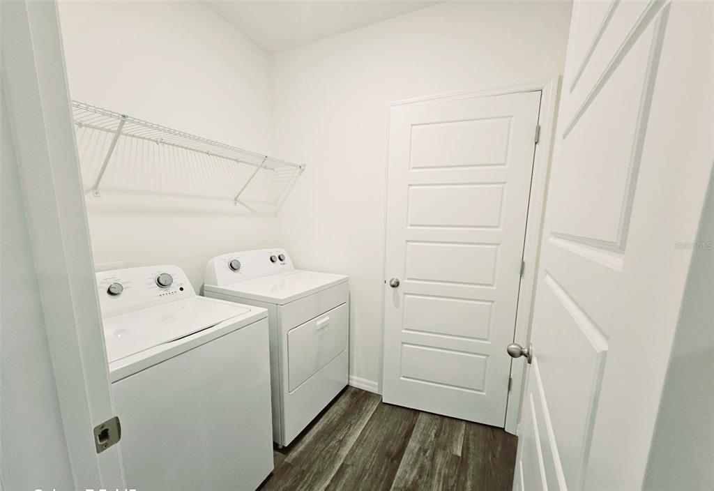 A laundry room features white appliances, a wire shelf, and wood-look flooring — 1237 LIMBALI STREET, MOUNT DORA, FL