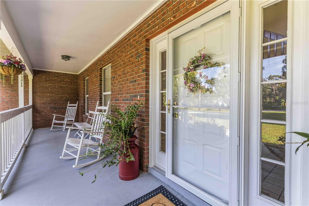 A covered brick porch features two white rocking chairs, a potted plant, and a front door — 9308 65TH AVENUE E, BRADENTON, FL