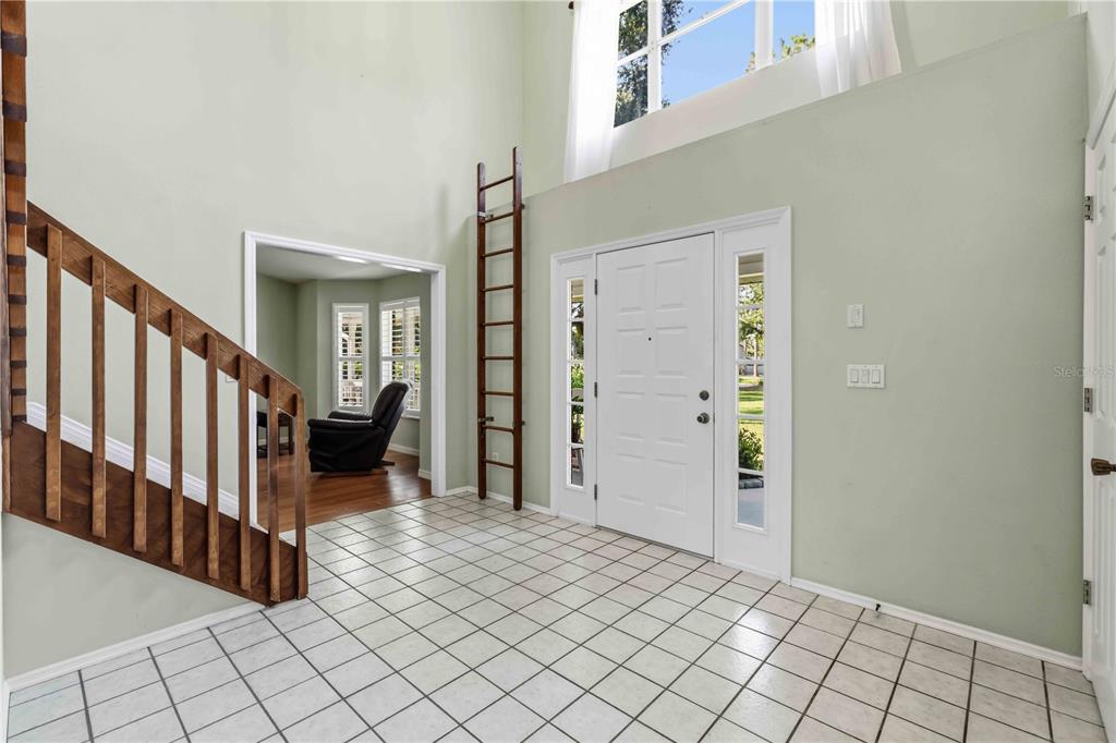 A two-story foyer features white tile flooring, a wooden staircase, and a tall decorative ladder — 9308 65TH AVENUE E, BRADENTON, FL