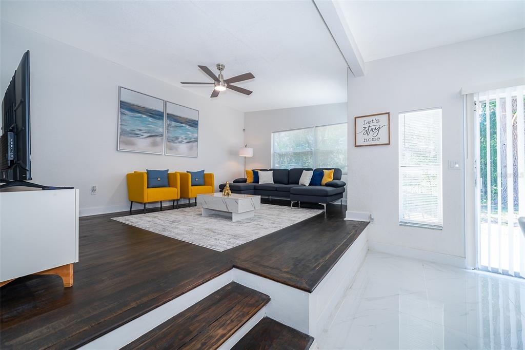 A sunken living room features dark wood flooring, a gray sectional, and two yellow chairs — 5815 WOLF ROAD, ORLANDO, FL