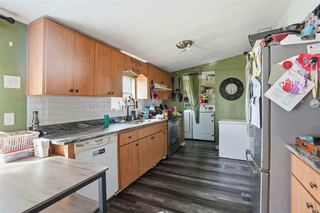 A kitchen with wood cabinets, granite countertops, white subway tile backsplash, and dark wood flooring — 8604 CAMEO DRIVE, NEW PORT RICHEY, FL