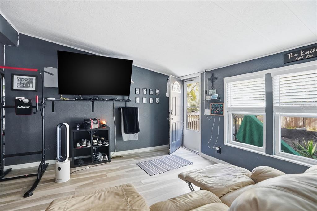 A living room features dark gray walls, light wood-look flooring, a wall-mounted television, and a recliner — 8604 CAMEO DRIVE, NEW PORT RICHEY, FL