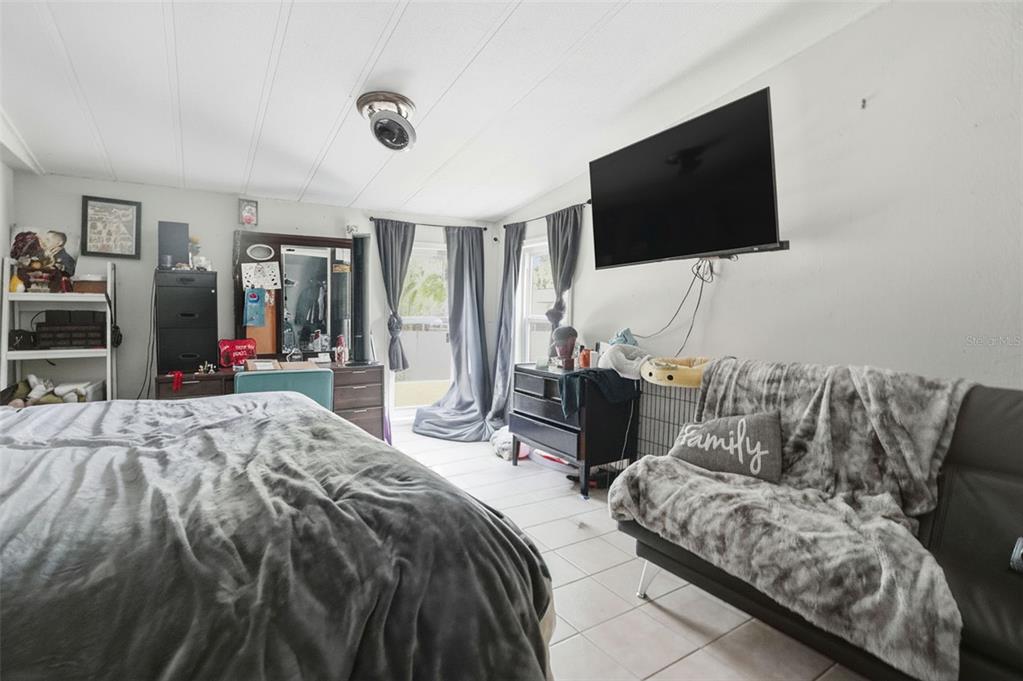A bedroom features a bed, a small sofa, a wall-mounted television, and a sliding glass door — 8604 CAMEO DRIVE, NEW PORT RICHEY, FL