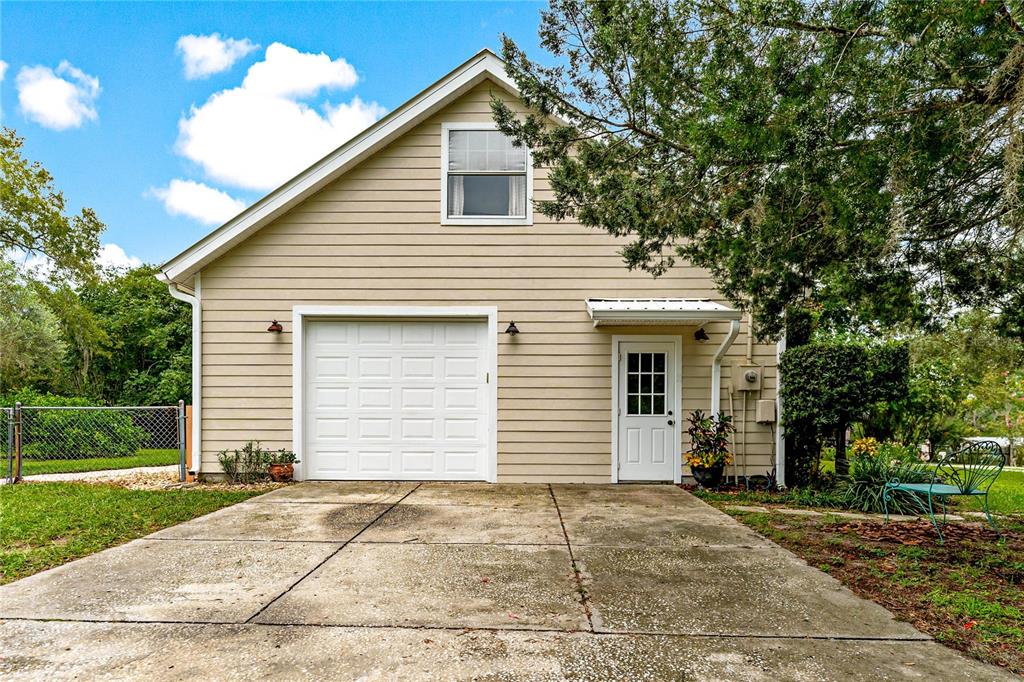 A detached garage with beige siding, a single white door, and a concrete driveway — 29249 WILPAYNE ROAD, BROOKSVILLE, FL