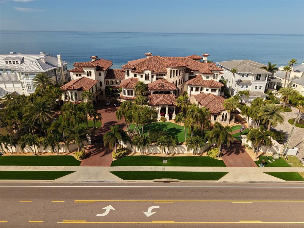 An aerial view shows a large Mediterranean-style mansion with a red tile roof near the ocean — 1700 GULF BOULEVARD, BELLEAIR BEACH, FL