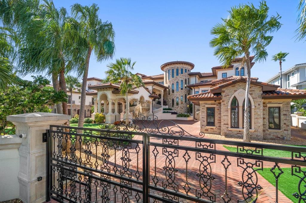A large stone mansion with a turret and palm trees behind a decorative iron gate — 1700 GULF BOULEVARD, BELLEAIR BEACH, FL
