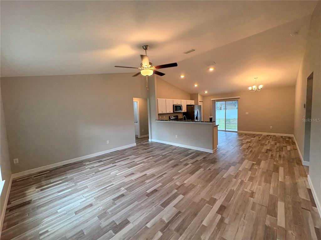 An open-concept living area features wood-look flooring, a vaulted ceiling, and a kitchen with white cabinets — 15705 SW 19TH AVENUE ROAD, OCALA, FL