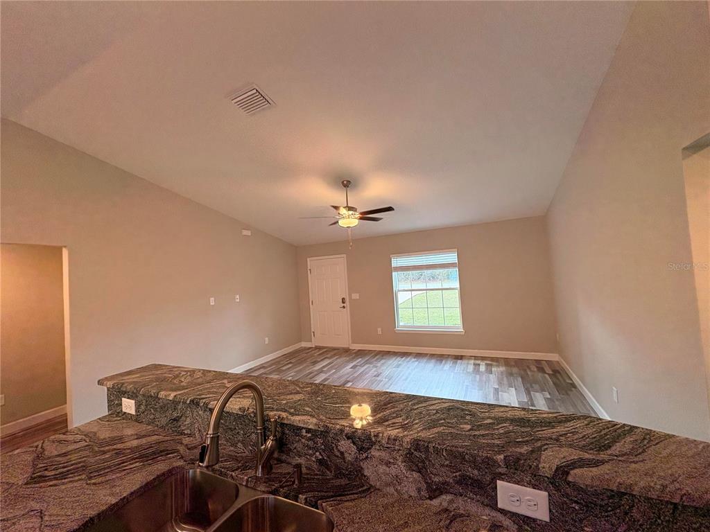 A kitchen with granite countertops overlooks an open living area with a ceiling fan — 15705 SW 19TH AVENUE ROAD, OCALA, FL