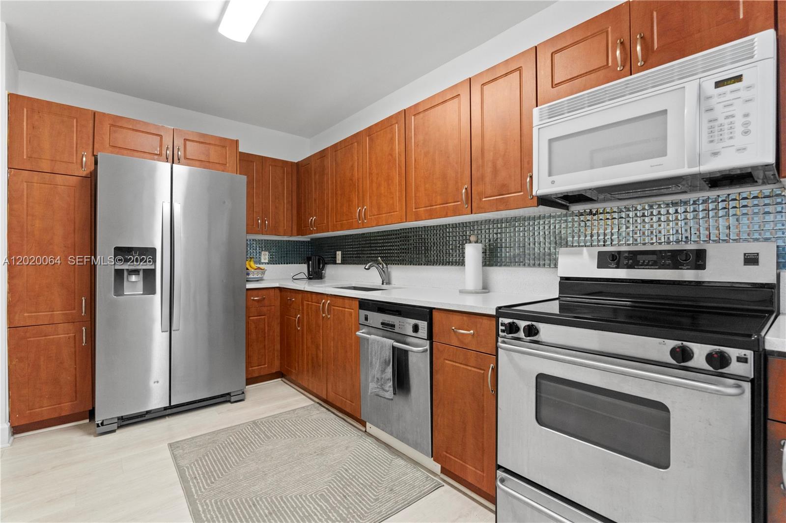 A kitchen features wood cabinets, stainless steel appliances, a white countertop, and a tiled backsplash — 401 69th St # 1509, Miami Beach FL 33141, MIAMI BEACH, FL