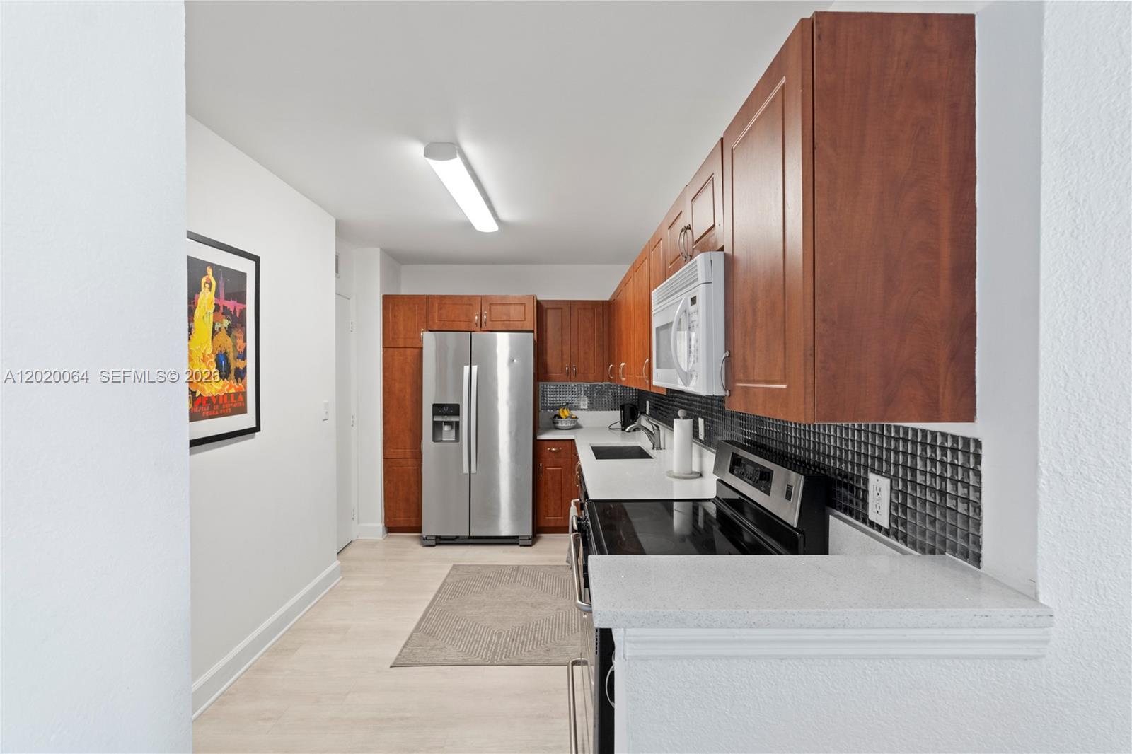 A kitchen features wood cabinets, stainless steel appliances, white countertops, and a black tiled backsplash — 401 69th St # 1509, Miami Beach FL 33141, MIAMI BEACH, FL