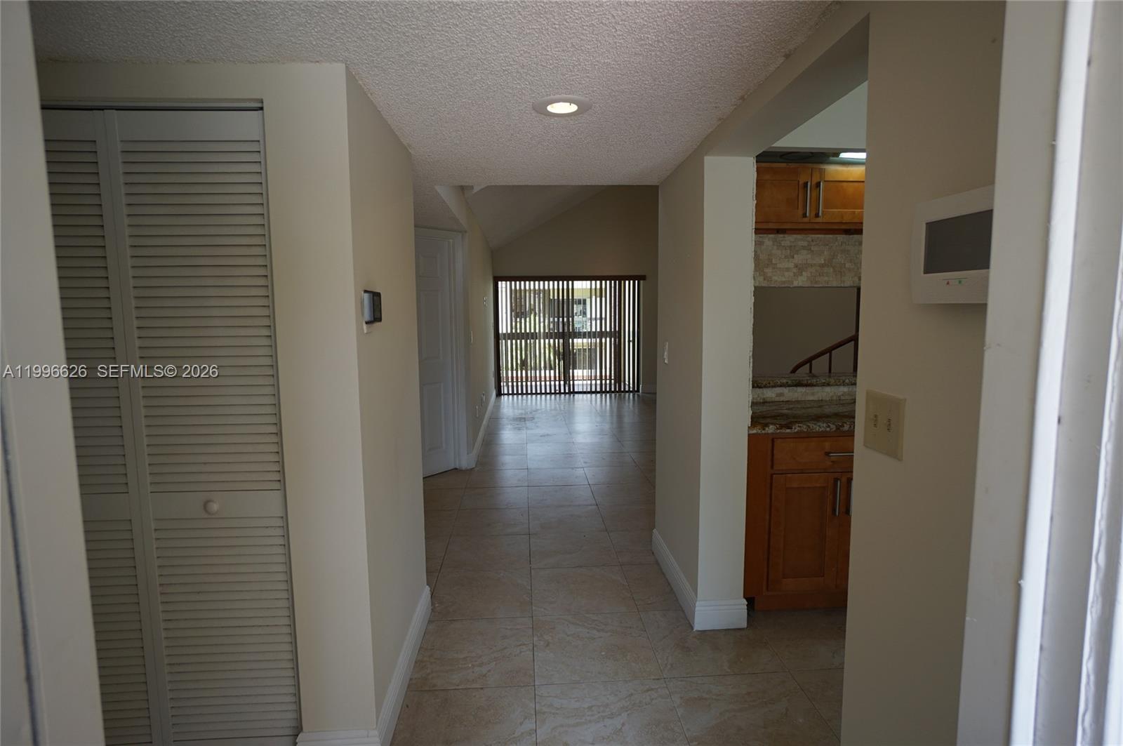 A hallway with tiled floors leads toward a living area with vertical blinds — 13015 SW 88th Ter S # B, Miami FL 33186, MIAMI, FL
