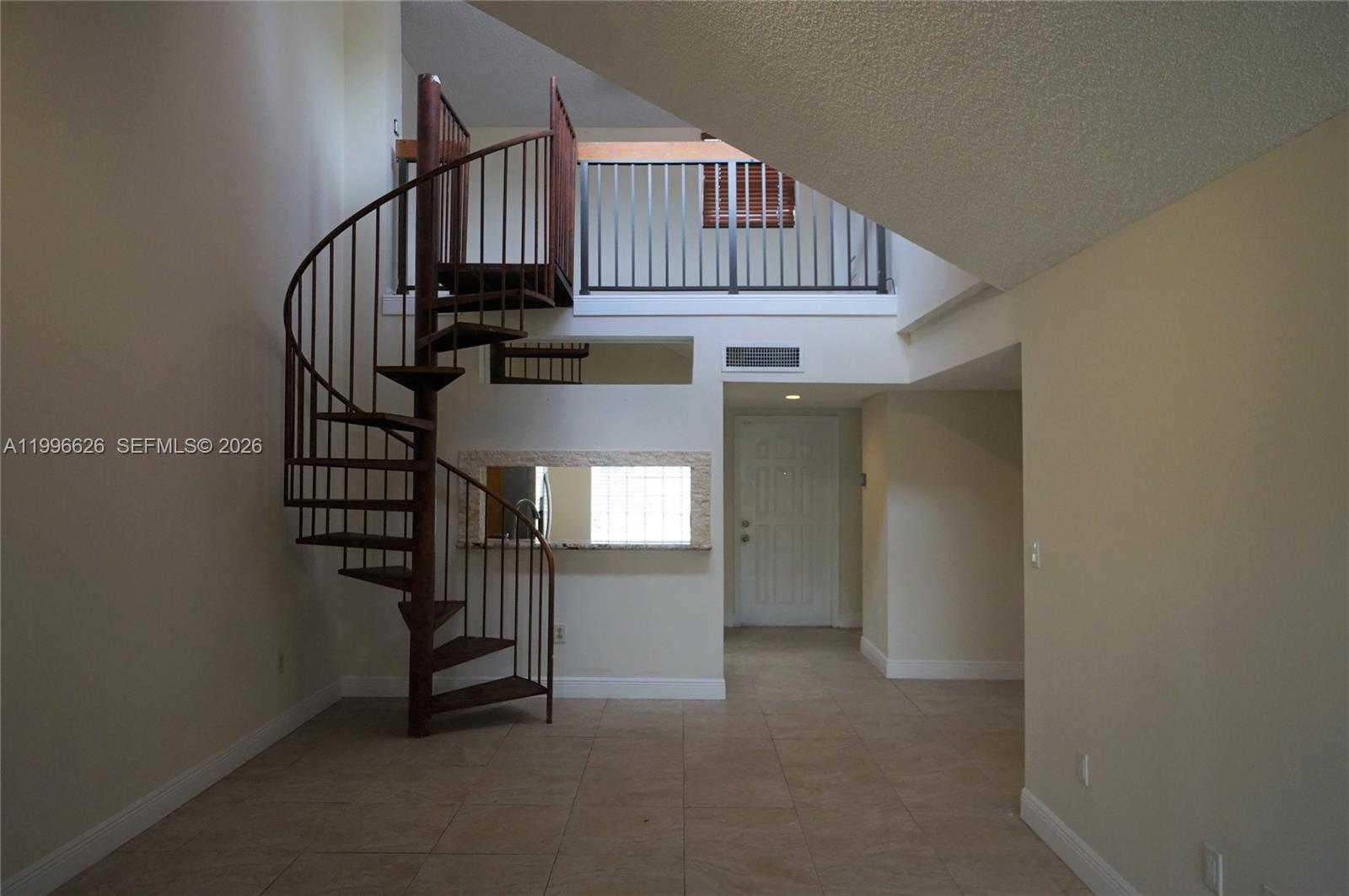 A spiral staircase stands in a tiled room with a loft railing and doorway — 13015 SW 88th Ter S # B, Miami FL 33186, MIAMI, FL