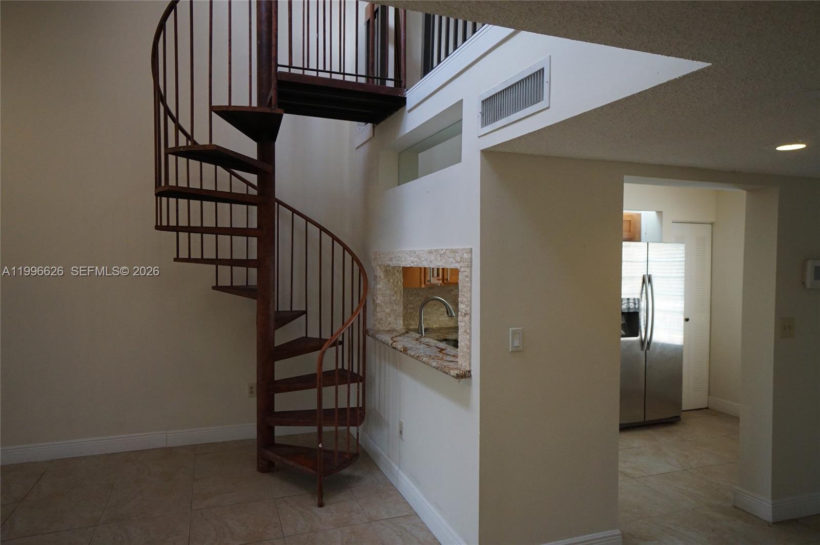 A spiral staircase stands next to a kitchen pass-through window in a tiled room — 13015 SW 88th Ter S # B, Miami FL 33186, MIAMI, FL
