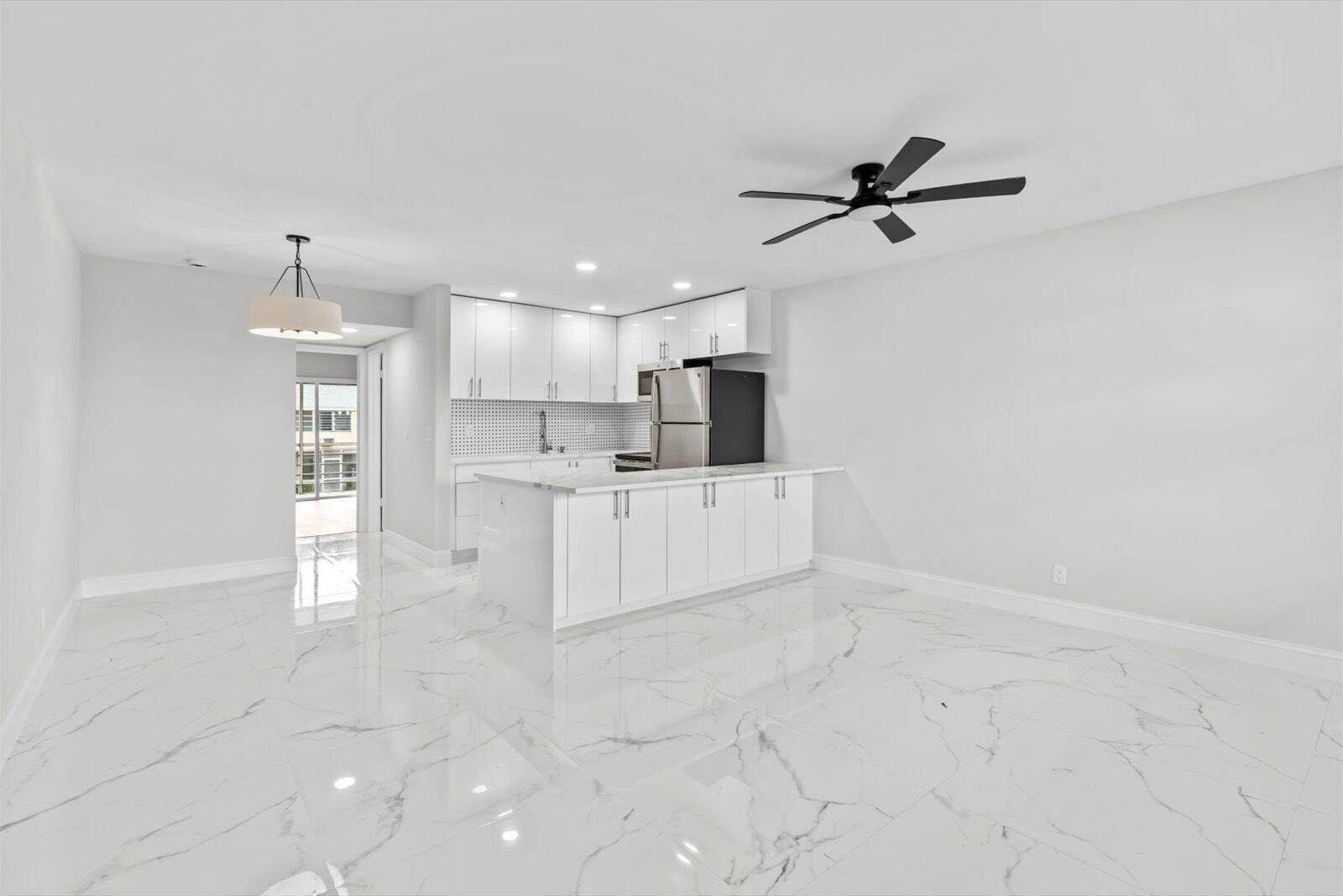 A modern kitchen with white cabinets and a marble-tiled floor opens into a living area — 17 Andover A, West Palm Beach FL 33417, WEST PALM BEACH, FL