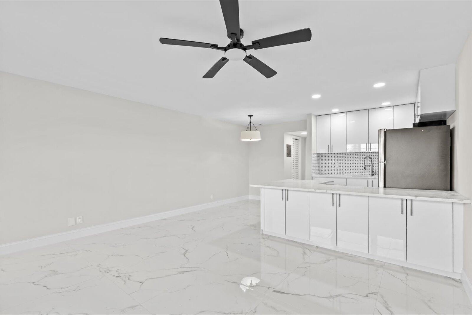 A modern kitchen with white cabinetry and a marble-topped island opens to a dining area — 17 Andover A, West Palm Beach FL 33417, WEST PALM BEACH, FL
