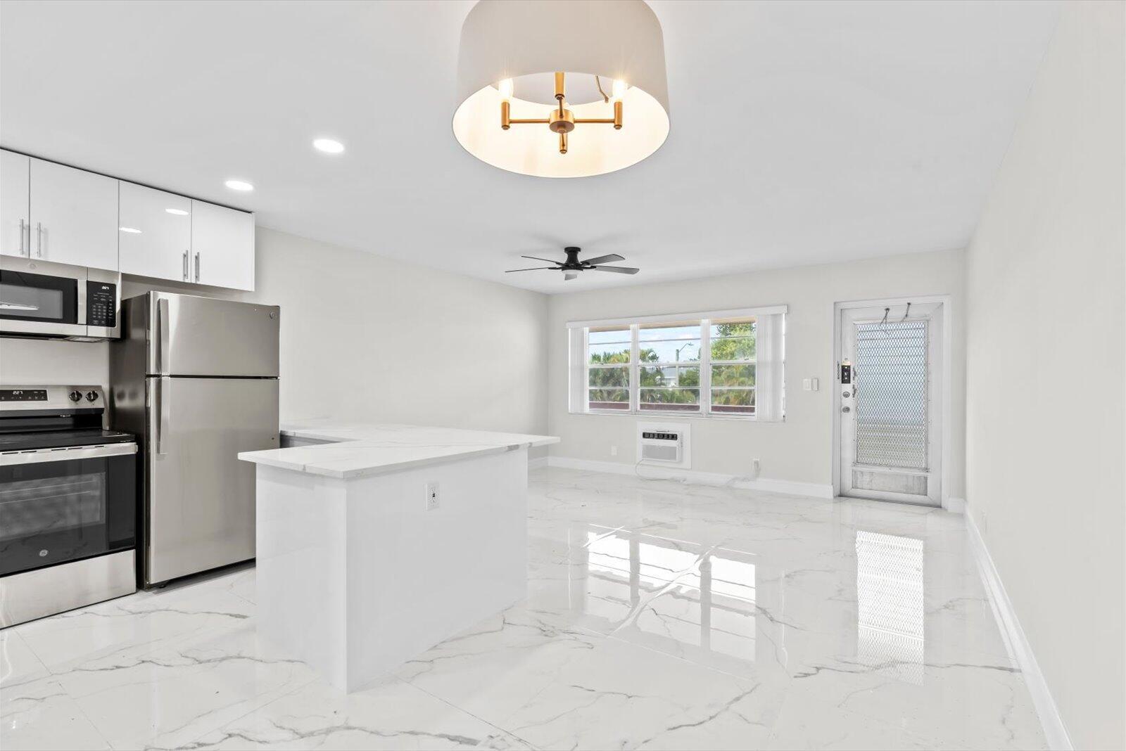 A kitchen and living area with white marble-look tile floors, stainless appliances, and a peninsula — 17 Andover A, West Palm Beach FL 33417, WEST PALM BEACH, FL