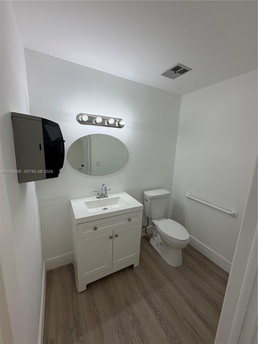 A small bathroom features a white vanity, an oval mirror, and a toilet with a grab bar — 503 SW 12th Ave, Miami FL 33130, MIAMI, FL