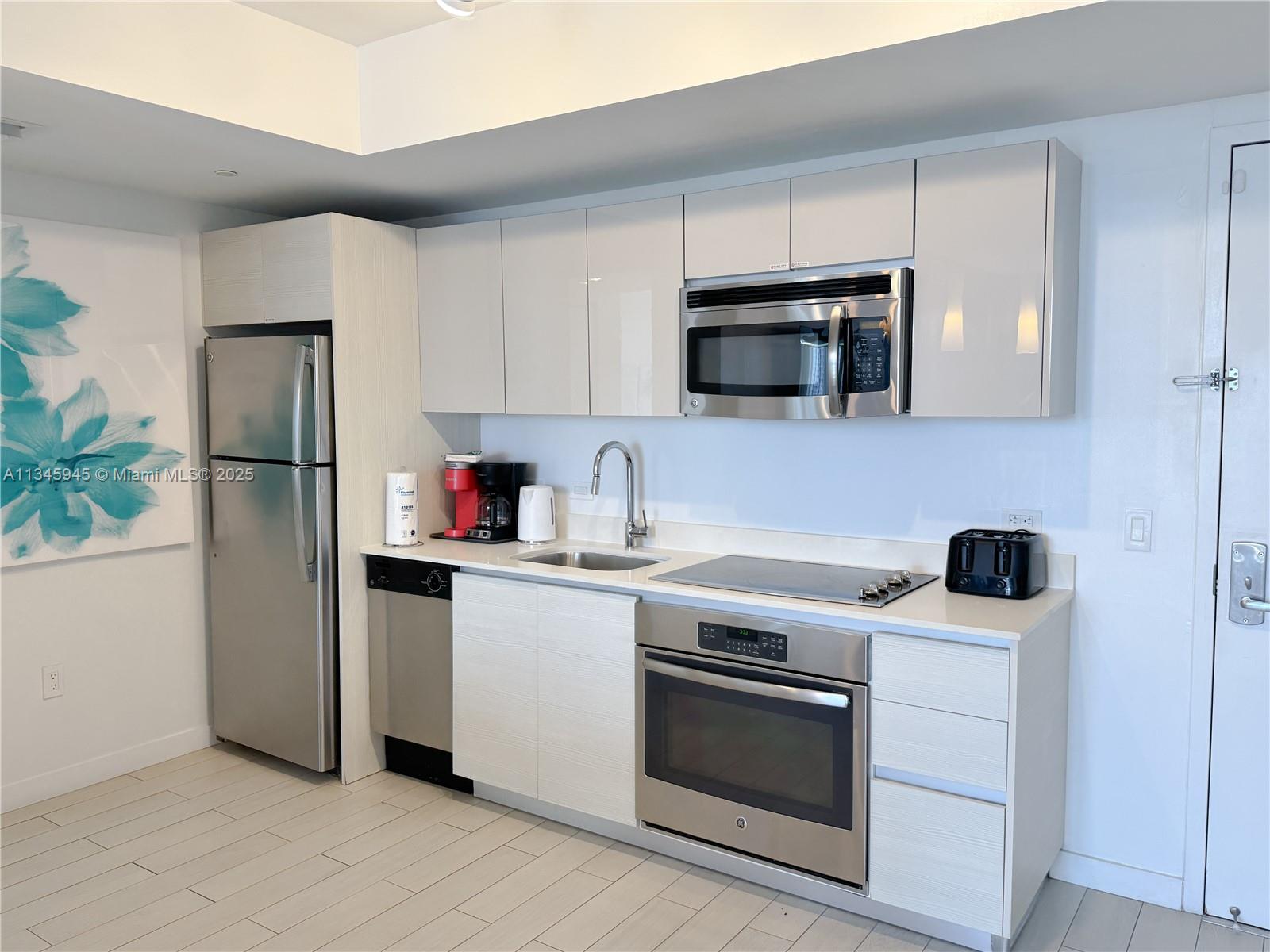 A modern kitchen features stainless steel appliances, white cabinetry, and light-colored tile flooring — 2602 E HALLANDALE BEACH BLVD # R1409, Hallandale Beach FL 33009, HALLANDALE BEACH, FL