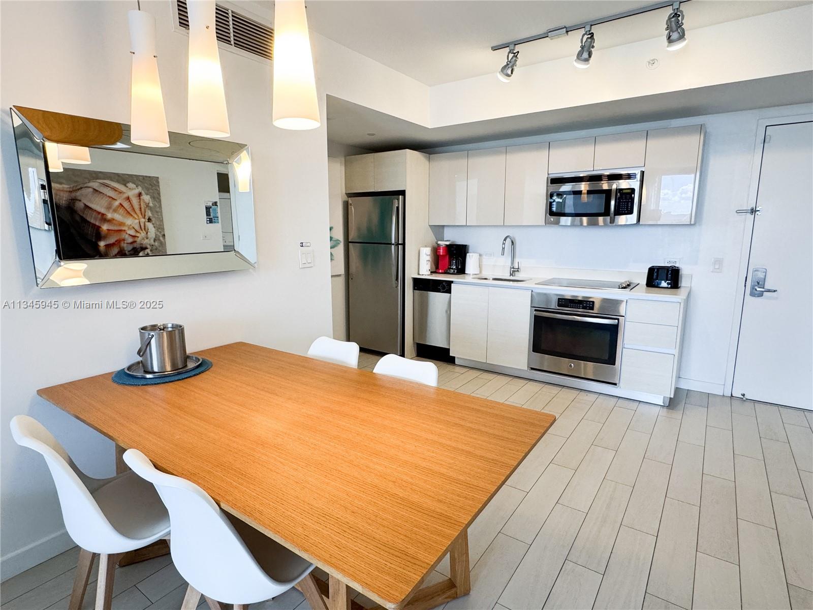 A dining area with a wooden table sits adjacent to a modern kitchen with stainless appliances — 2602 E HALLANDALE BEACH BLVD # R1409, Hallandale Beach FL 33009, HALLANDALE BEACH, FL
