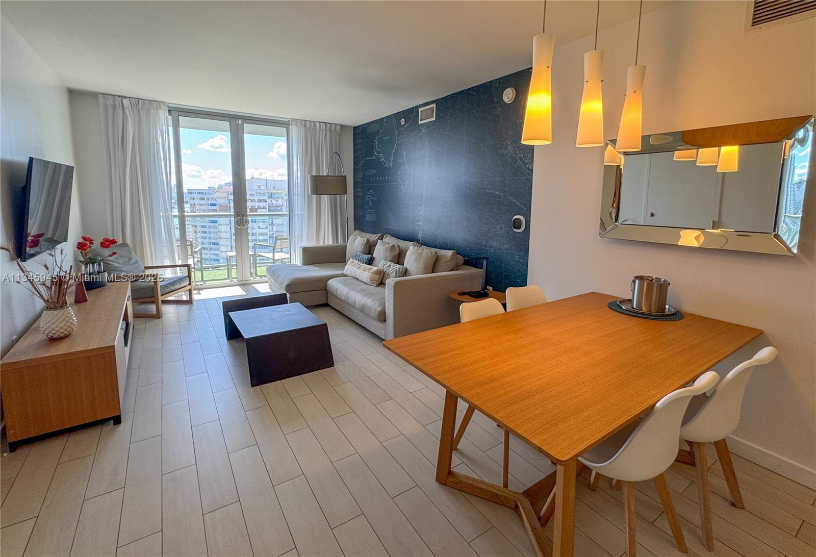 A living and dining area features a map-patterned accent wall, light tile floors, and balcony — 2602 E HALLANDALE BEACH BLVD # R1409, Hallandale Beach FL 33009, HALLANDALE BEACH, FL