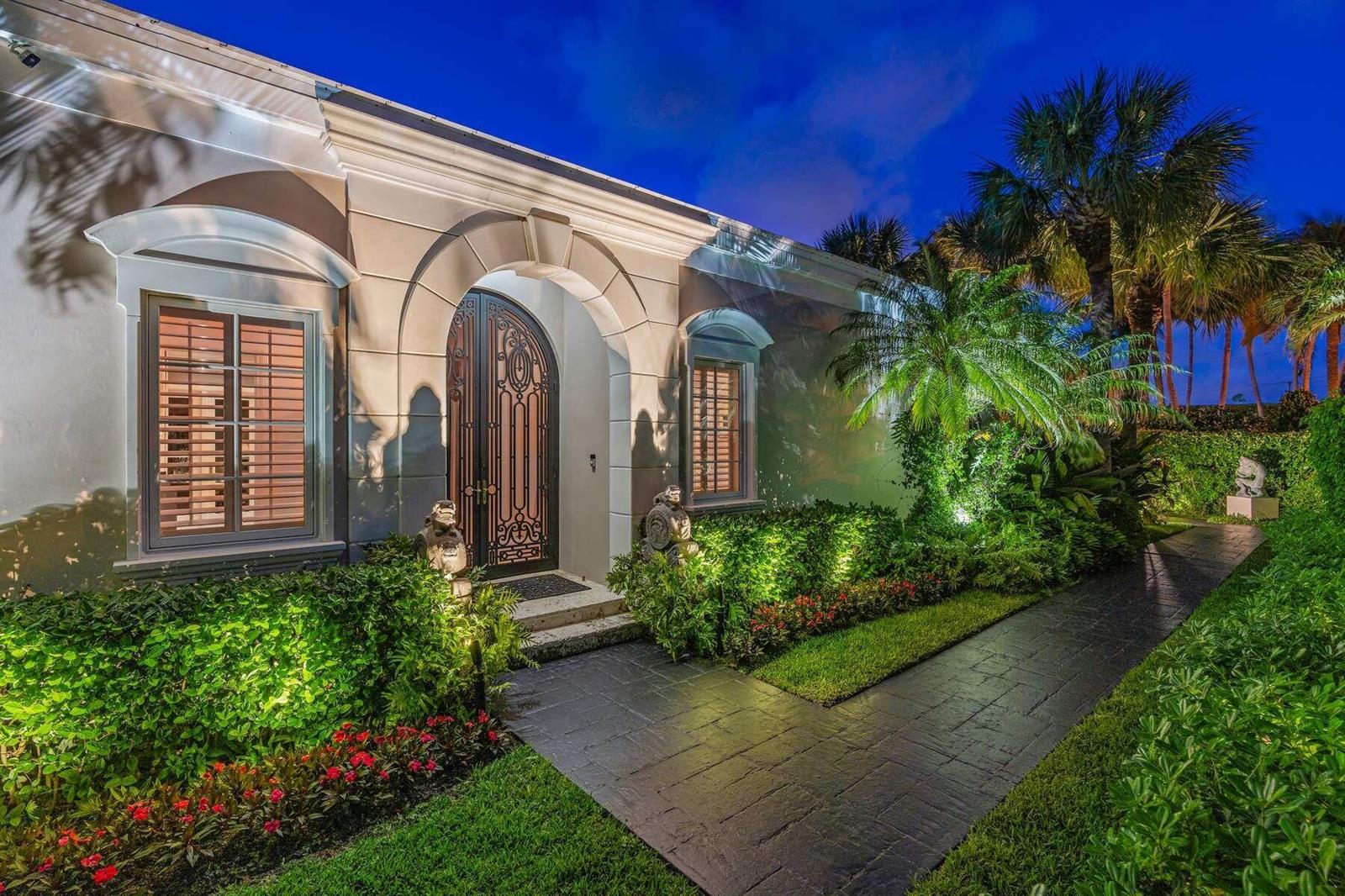 The exterior of a house at night features an arched doorway, landscaping, and stone walkway — 710 N COUNTY Road, Palm Beach FL 33480, PALM BEACH, FL