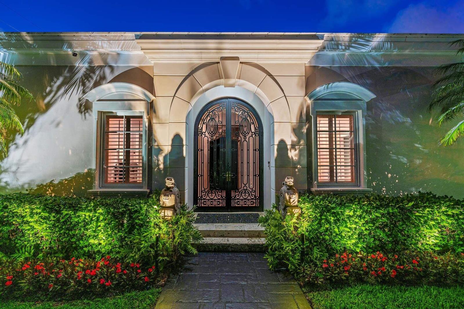 The exterior of a house features an arched iron front door flanked by two windows — 710 N COUNTY Road, Palm Beach FL 33480, PALM BEACH, FL