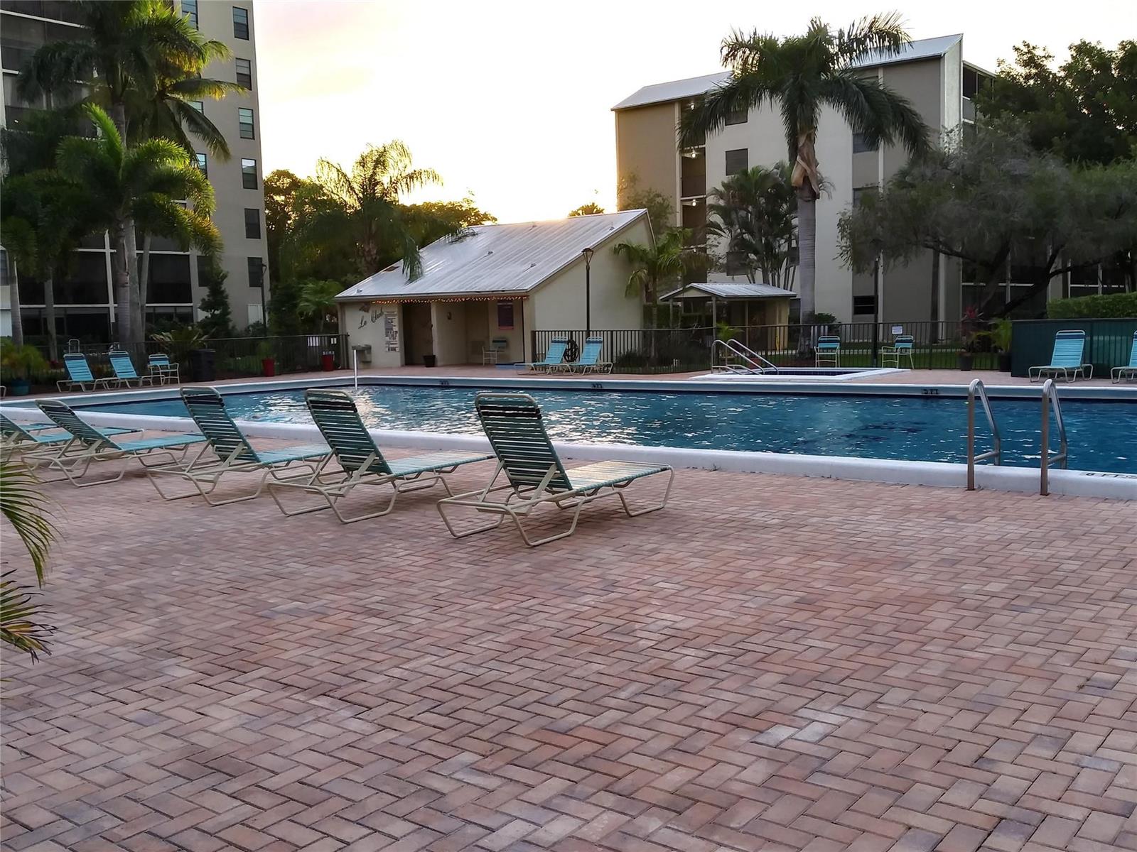 A swimming pool with lounge chairs on a brick patio surrounded by apartment buildings — 2112 S Cypress Bend Drive # 207, Pompano Beach FL 33069, POMPANO BEACH, FL