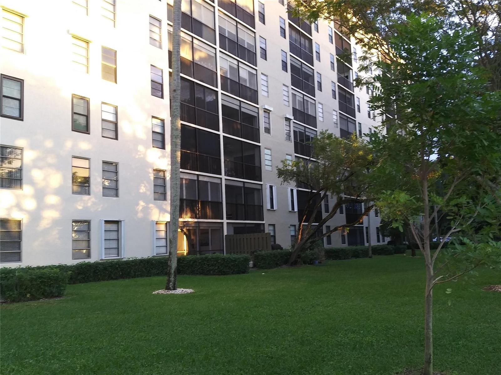 A multi-story apartment building with screened balconies stands next to a grassy lawn — 2112 S Cypress Bend Drive # 207, Pompano Beach FL 33069, POMPANO BEACH, FL