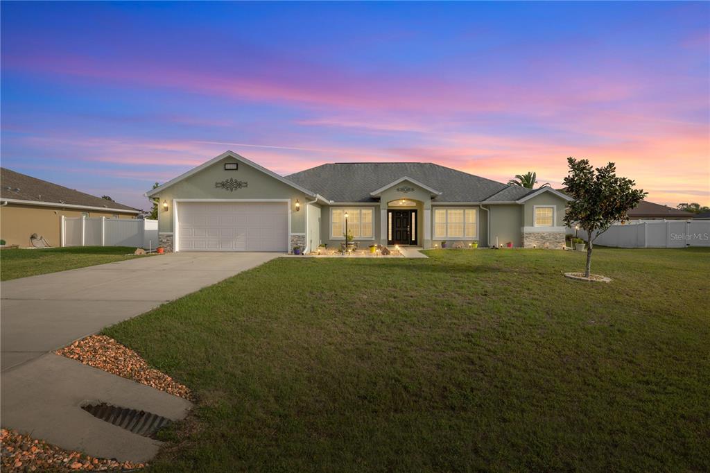 A single-story house with a light green exterior, a two-car garage, and a large lawn — 9957 SW 55TH AVENUE ROAD, OCALA, FL