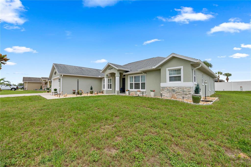 A single-story house with light green stucco siding, stone accents, and a gray shingled roof — 9957 SW 55TH AVENUE ROAD, OCALA, FL