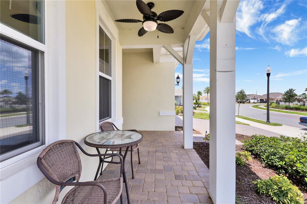 A covered front porch features a small bistro set, a ceiling fan, and paver flooring — 13175 SUNNY RETREAT LANE, WINTER GARDEN, FL
