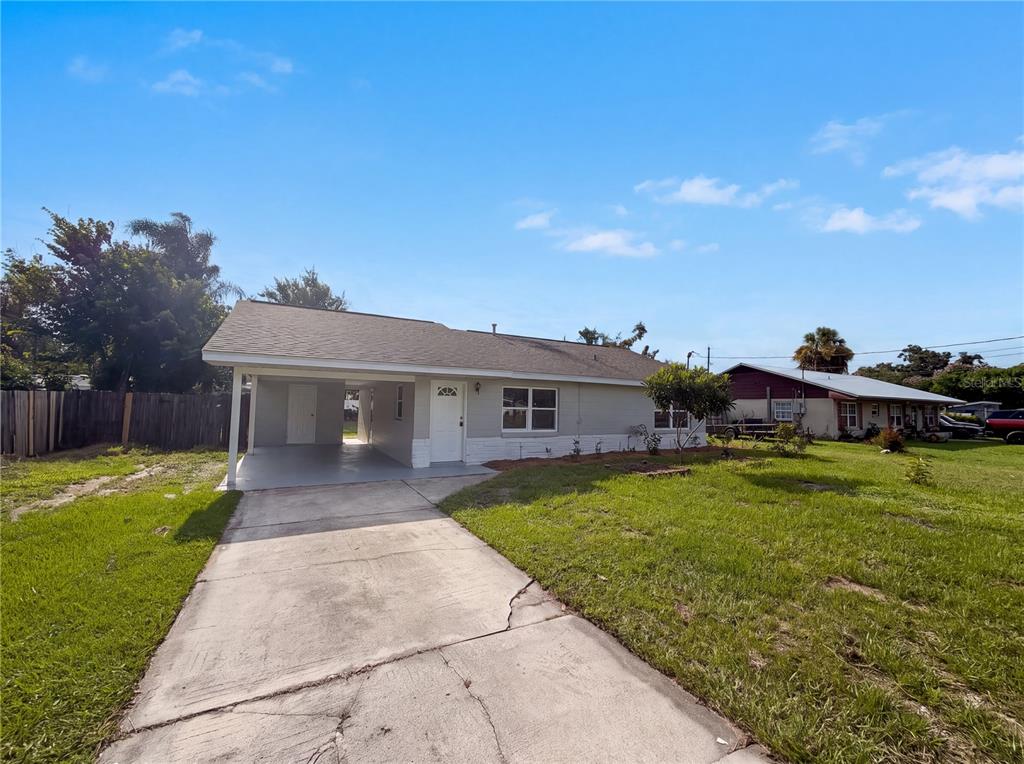 A single-story house with a carport, gray siding, and a concrete driveway under a blue sky — 2710 WOODLAWN DRIVE, WINTER HAVEN, FL