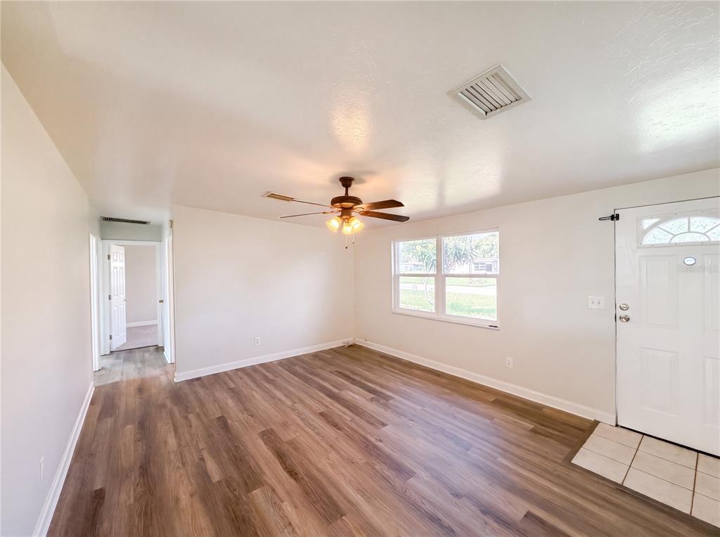 A living room with wood-look flooring, a ceiling fan, and a white front door — 2710 WOODLAWN DRIVE, WINTER HAVEN, FL