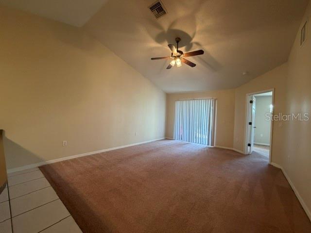 An empty living room features beige carpeting, a vaulted ceiling with a fan, and sliding doors — 31-33 E ST LOUIS AVENUE, EUSTIS, FL