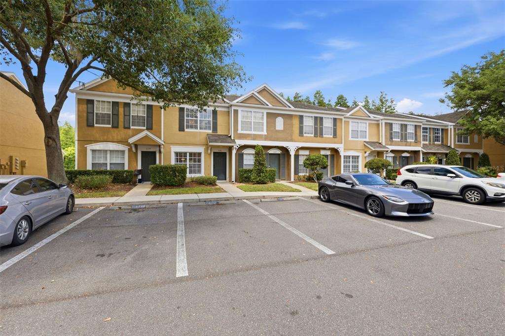 A row of two-story townhouses with tan stucco exteriors and a parking lot in front — 1141 KENNEWICK COURT, WESLEY CHAPEL, FL