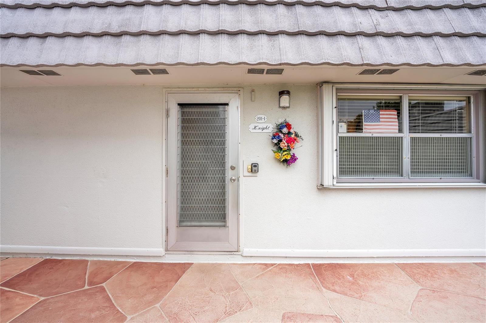 The exterior of a home features a white stucco wall, a glass door, and a window — 201 Valencia I, Delray Beach FL 33446, DELRAY BEACH, FL