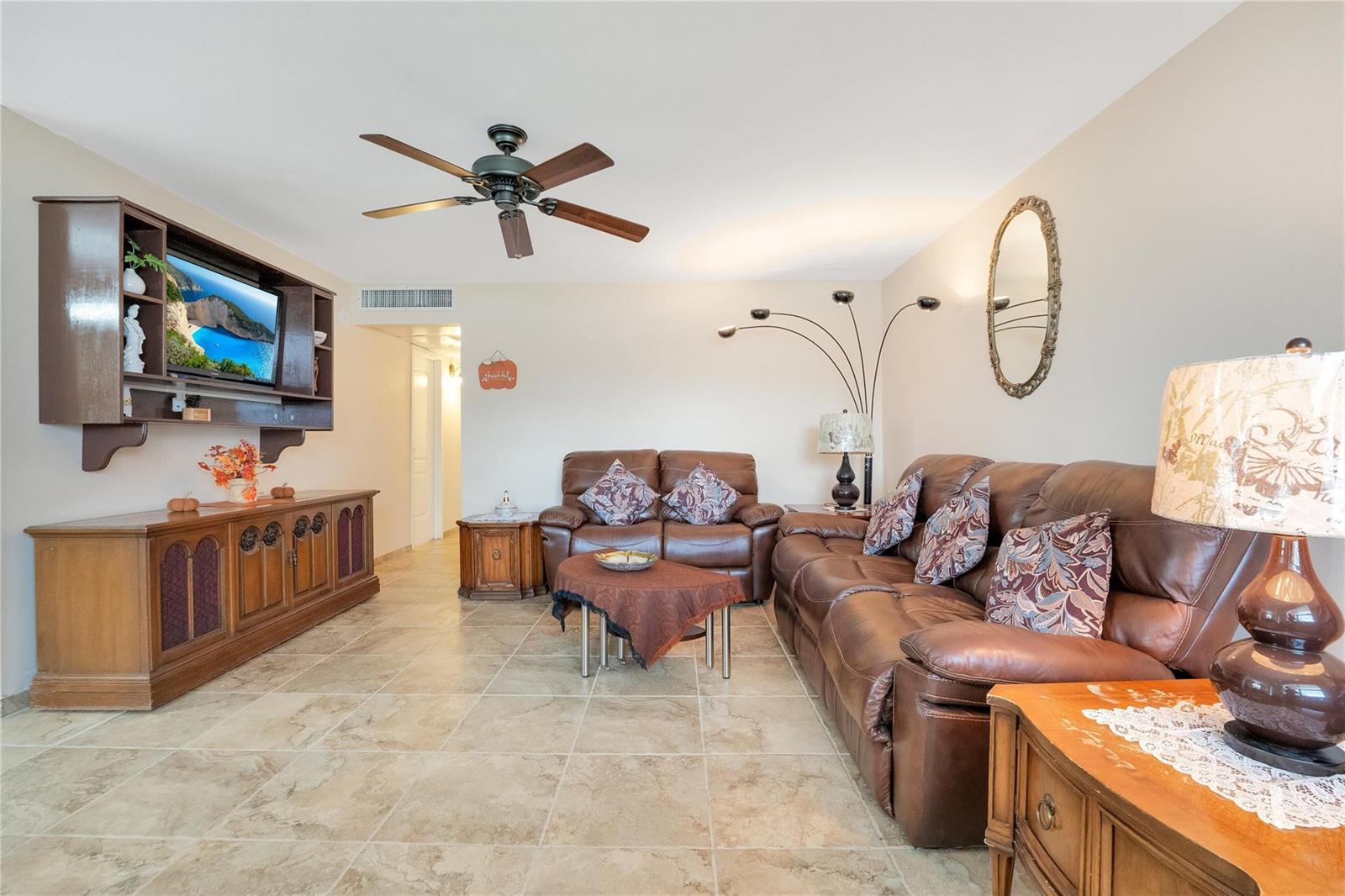 A living room features tile flooring, brown leather furniture, a ceiling fan, and wall-mounted cabinetry — 201 Valencia I, Delray Beach FL 33446, DELRAY BEACH, FL