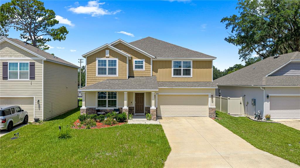 A two-story suburban house with tan siding, a stone-accented porch, and a two-car garage — 826 NW 244TH DRIVE, NEWBERRY, FL