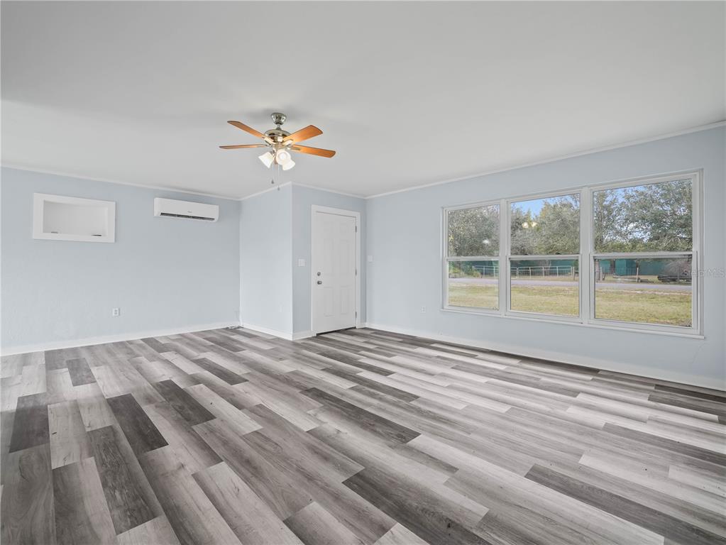 A living room features light blue walls, wood-look vinyl flooring, a ceiling fan, and large windows — 5926 VAN SIMMONS ROAD, WAUCHULA, FL