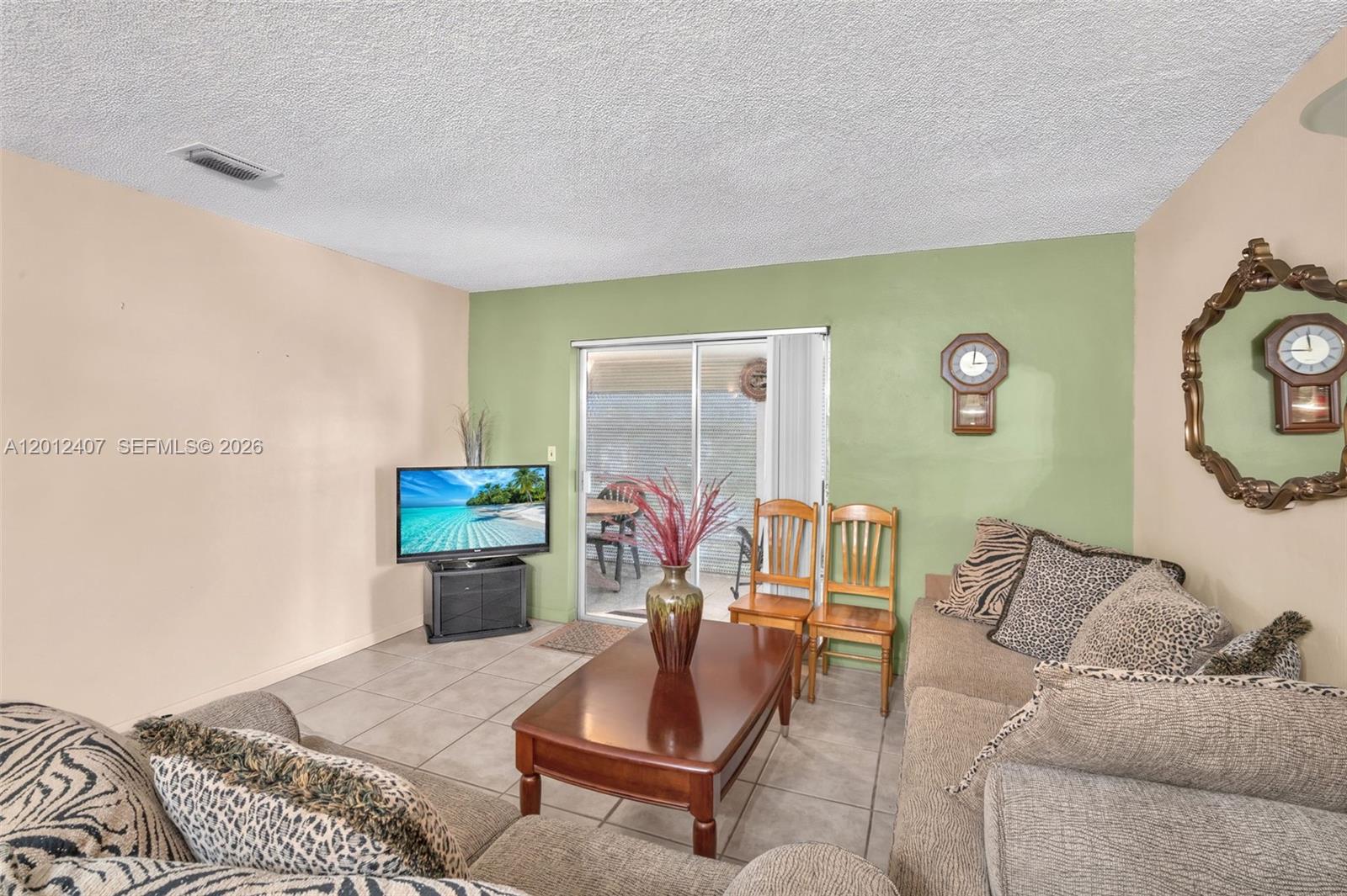 A living room features tile flooring, a green accent wall, and a sliding glass door — 16901 NE 13th Ave # 303, Miami FL 33162, MIAMI, FL