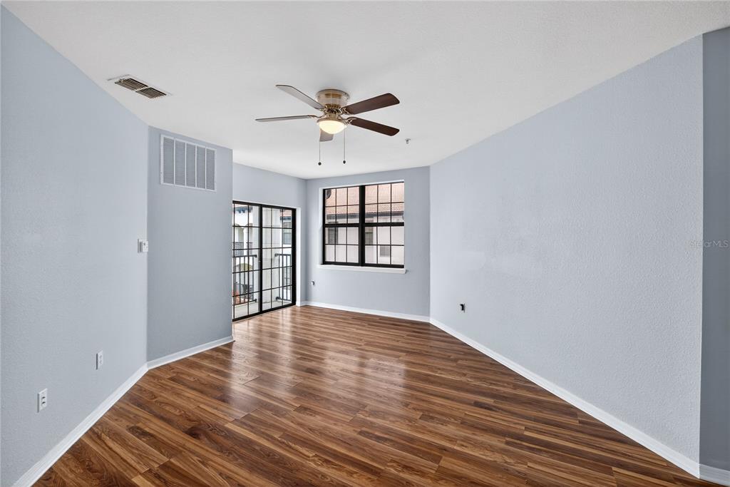An empty room features light blue walls, wood-look flooring, a ceiling fan, and sliding doors — 5550 E MICHIGAN STREET UNIT 3306, ORLANDO, FL