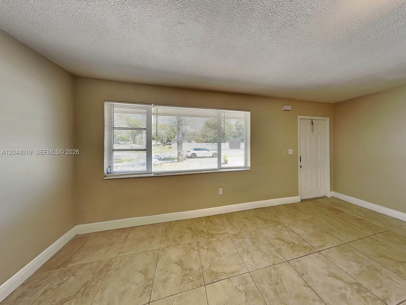 An empty room features beige walls, large windows with blinds, and light-colored tile flooring — SUNRISE, FL