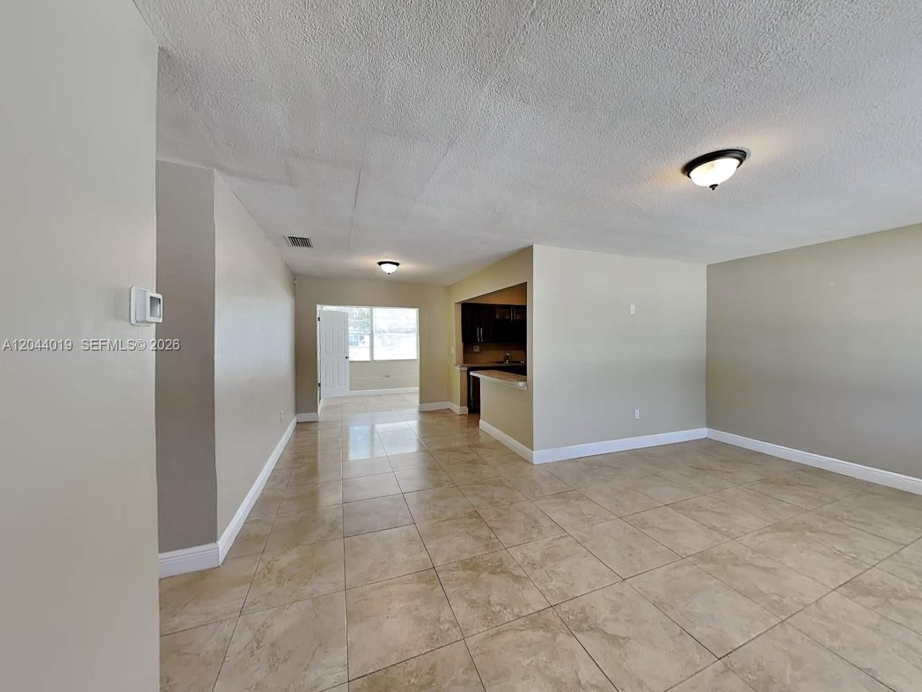 An open living area features beige tile flooring, neutral walls, and a kitchen pass-through window — SUNRISE, FL