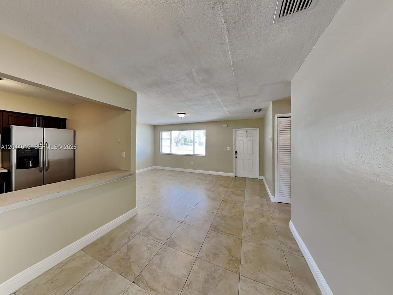 An open-concept living area features beige tile flooring, a kitchen pass-through, and a white door — SUNRISE, FL