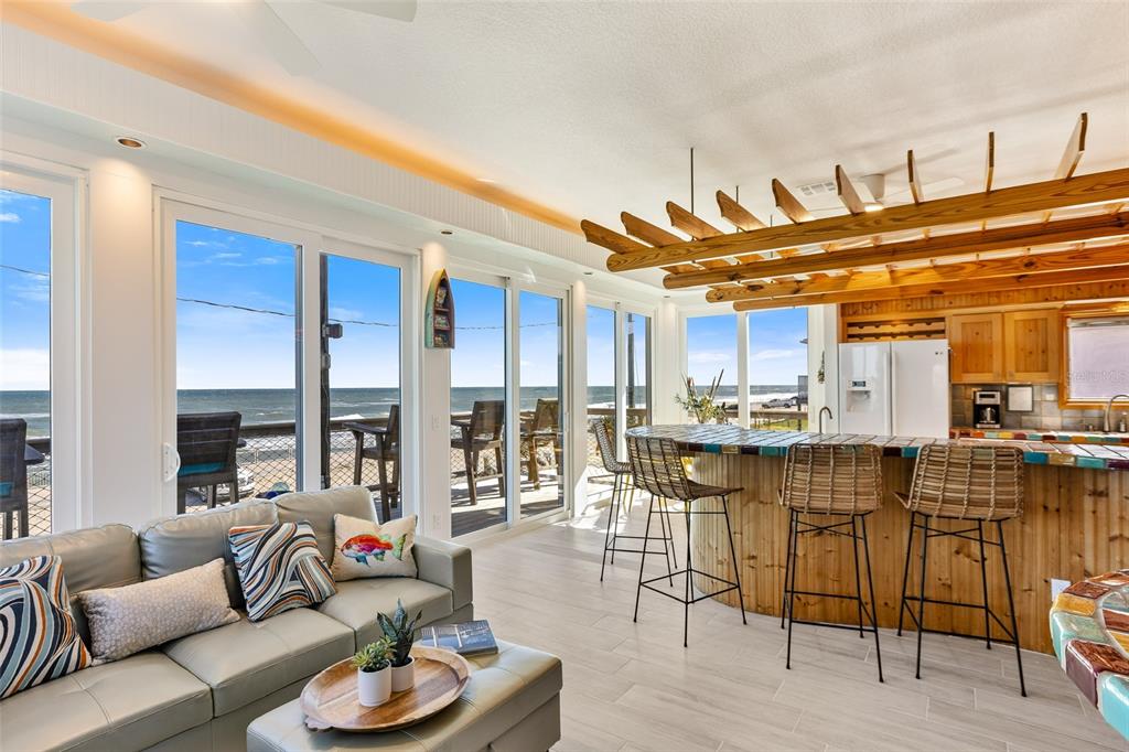 A living room and kitchen area with a bar, wooden ceiling beams, and ocean views — 6618 S ATLANTIC AVENUE, NEW SMYRNA BEACH, FL