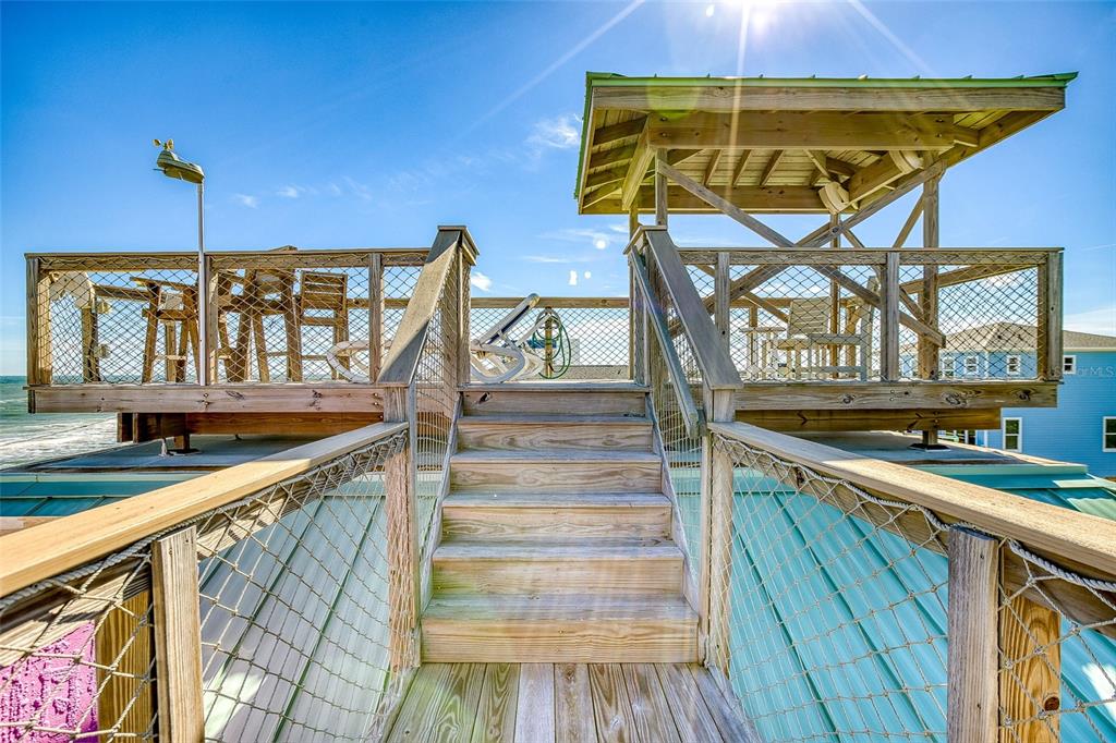 A wooden rooftop deck features a covered seating area, stairs, and metal safety railings — 6618 S ATLANTIC AVENUE, NEW SMYRNA BEACH, FL