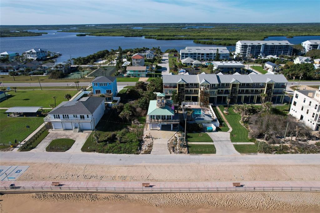 An aerial view shows beachfront homes and multi-story residential buildings along a coastal road — 6618 S ATLANTIC AVENUE, NEW SMYRNA BEACH, FL